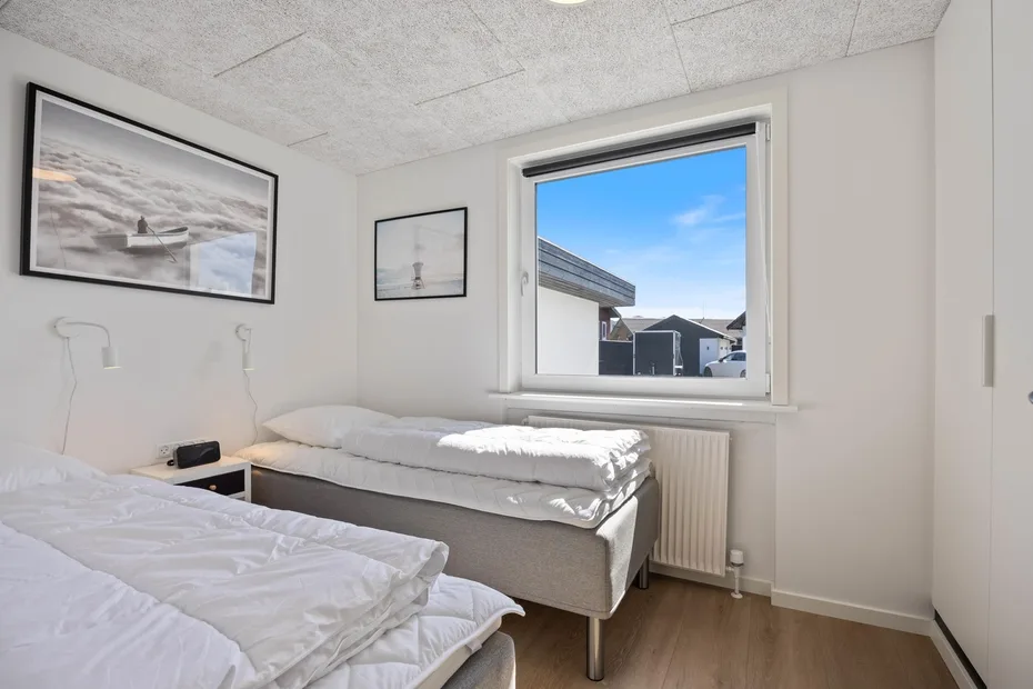 Un dormitorio luminoso con dos camas y una ventana con vista a edificios cercanos.