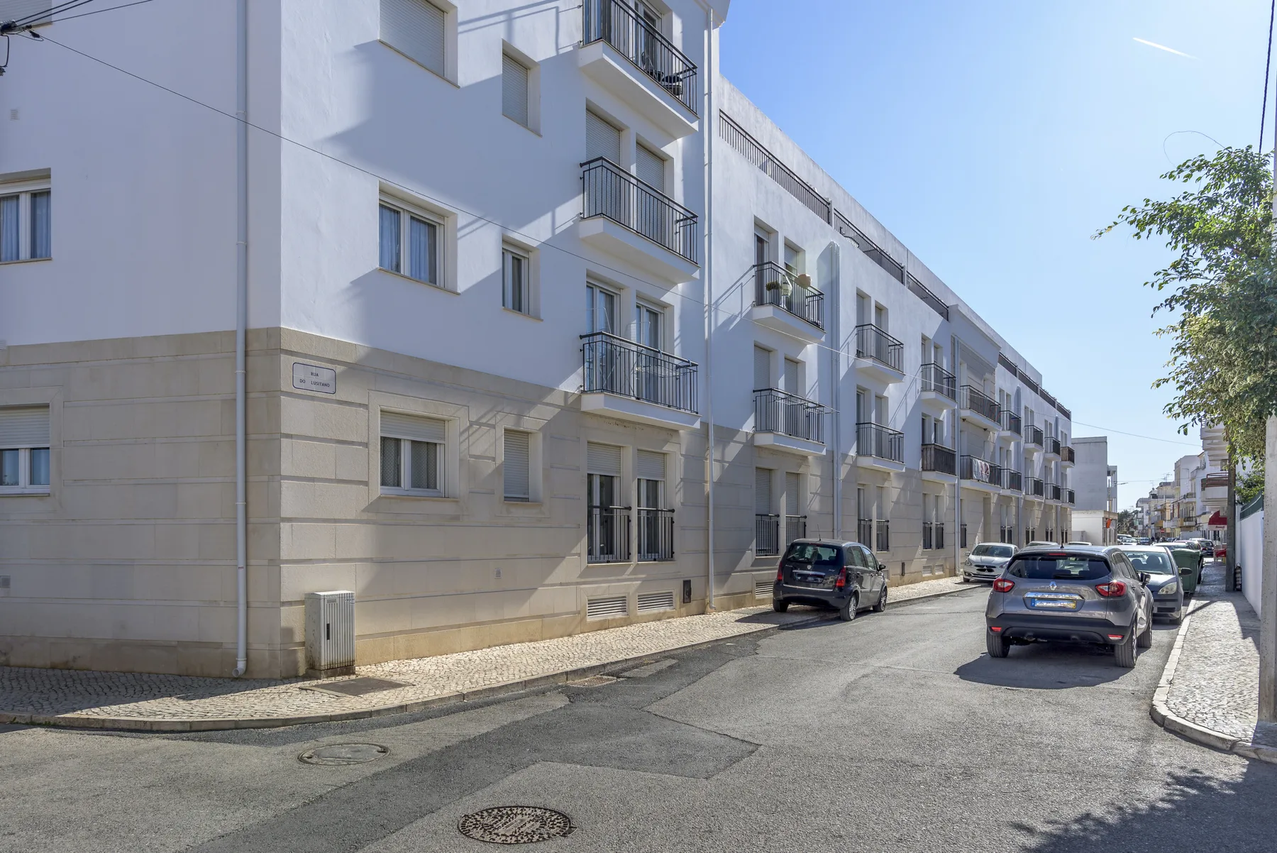 A residential street lined with apartment buildings and parked cars.