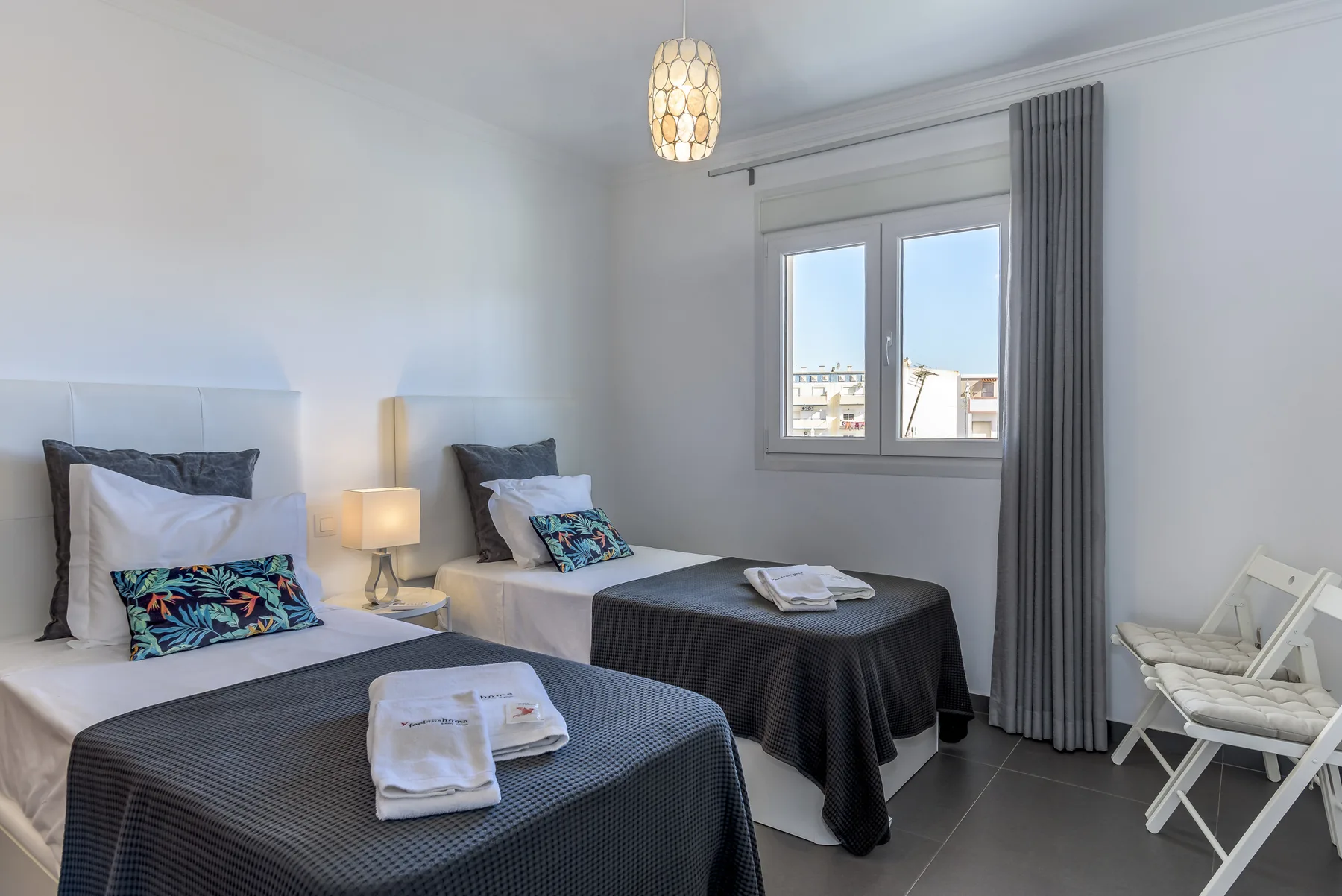 A bright bedroom with two single beds, bedside lamps, and a window.