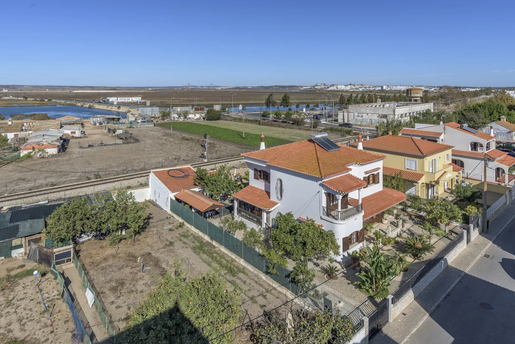 Aerial view of a white house with terracotta roofs beside a road.