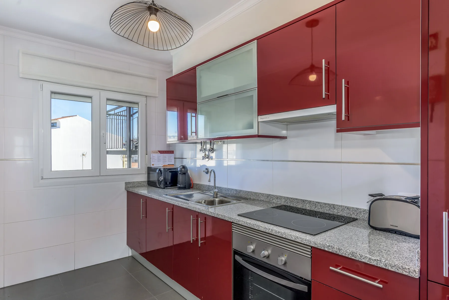 A bright kitchen with red cabinets, a countertop, and a window.