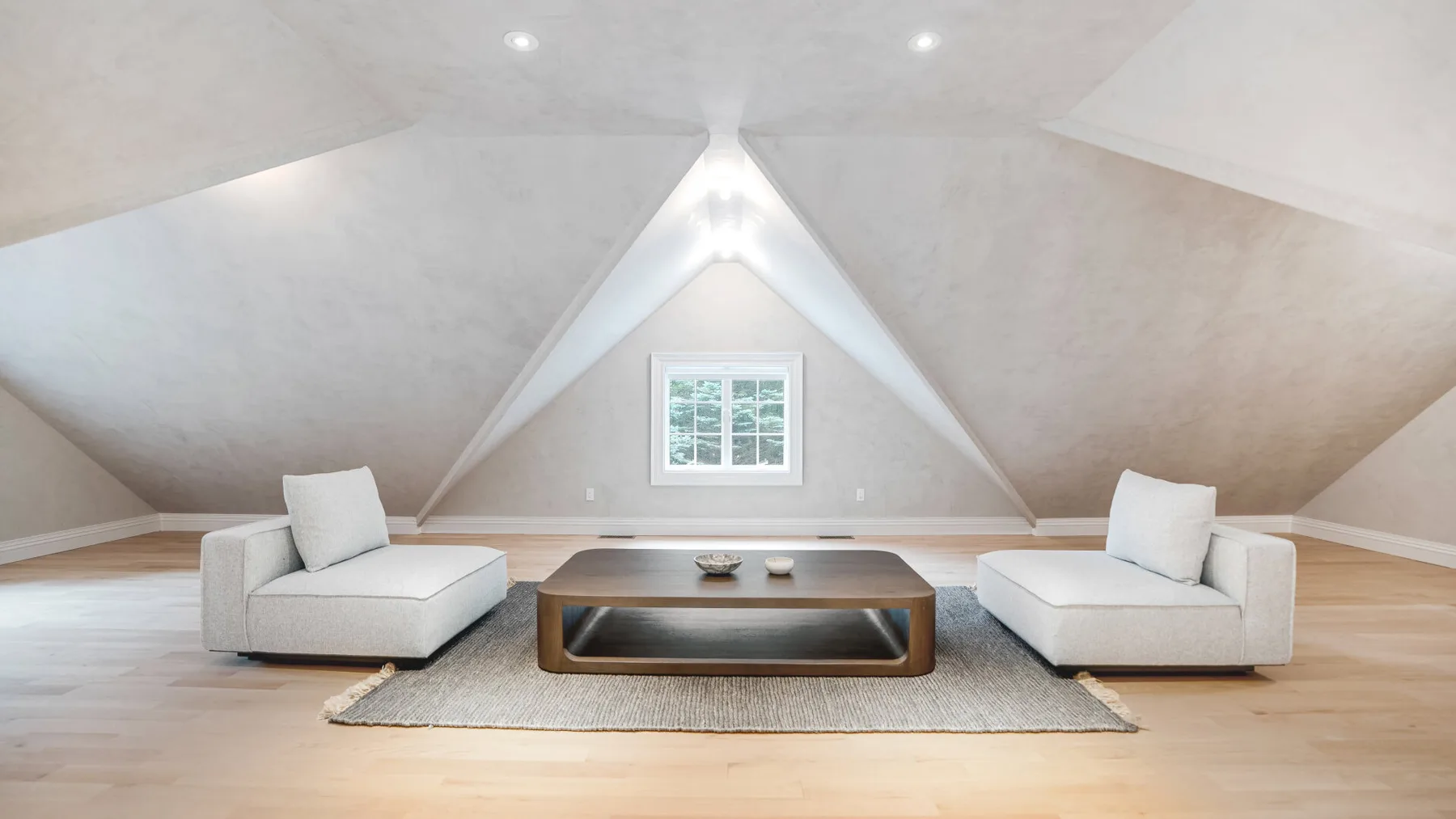 Una luminosa sala de estar en el ático con dos asientos y una mesa baja bajo una ventana.