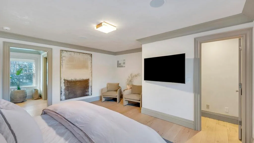 Un dormitorio con una cama, dos asientos y un televisor montado en la pared.