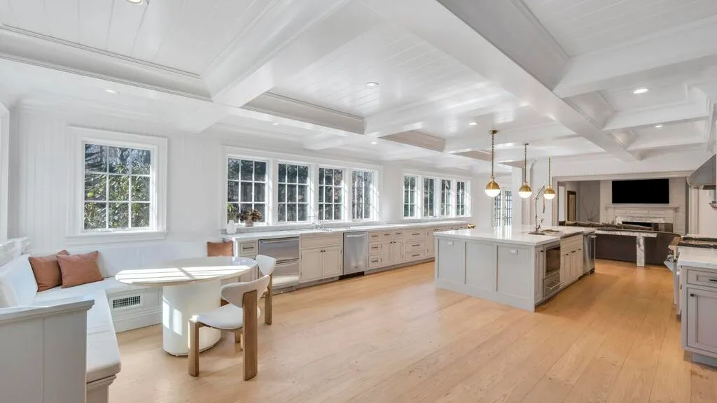 Una cocina luminosa con una isla central, gabinetes claros y una pequeña mesa de comedor.