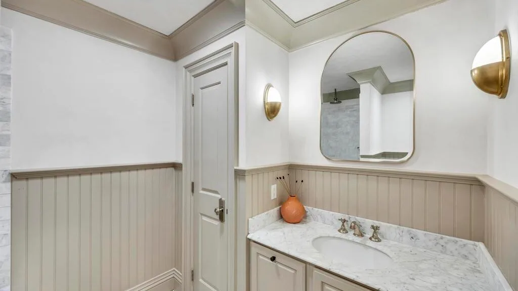 Un lavabo de baño con encimera de mármol, fregadero y espejo arqueado.