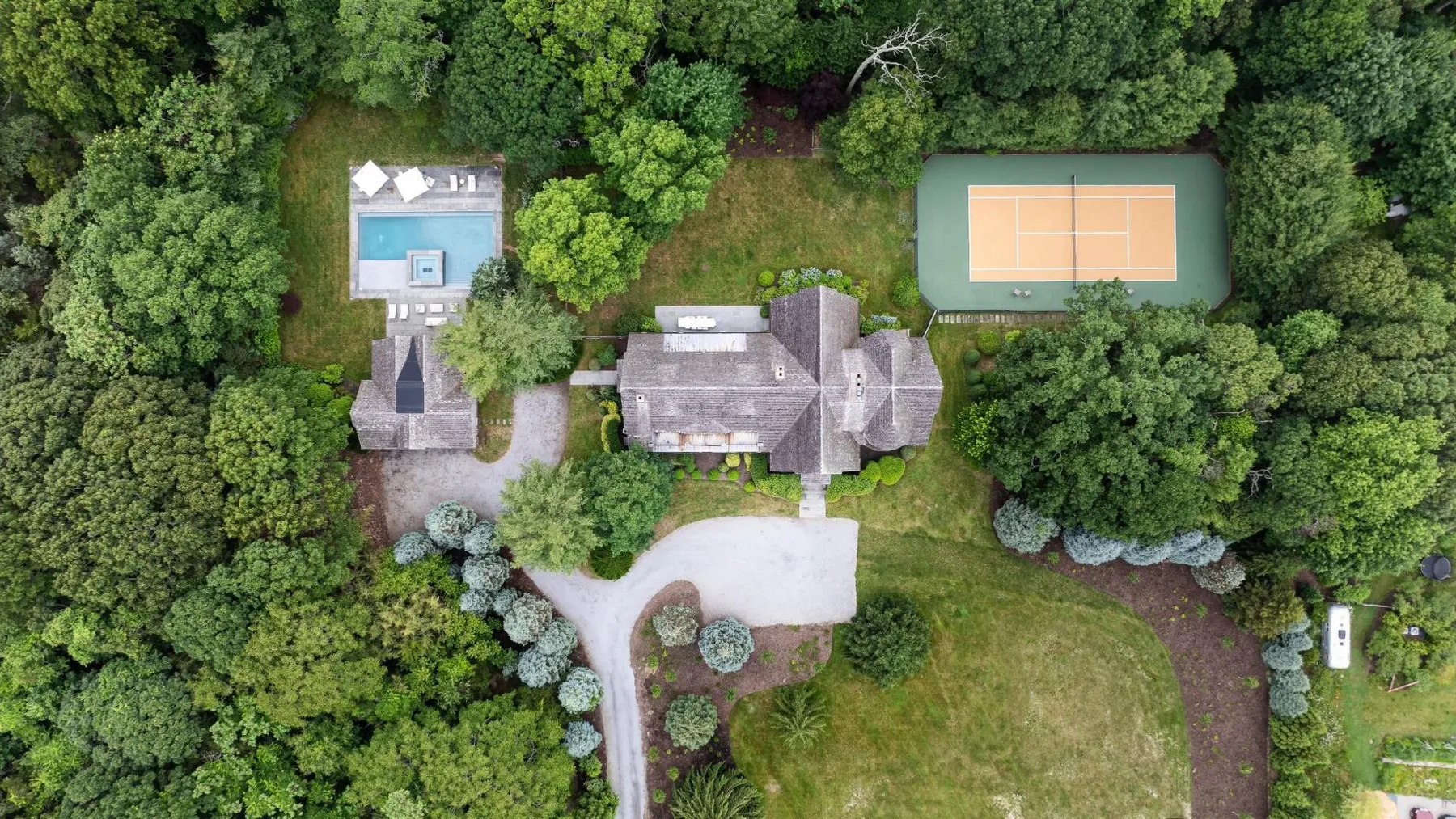 Vista aérea de una propiedad arbolada con una casa, una piscina y una cancha de tenis.