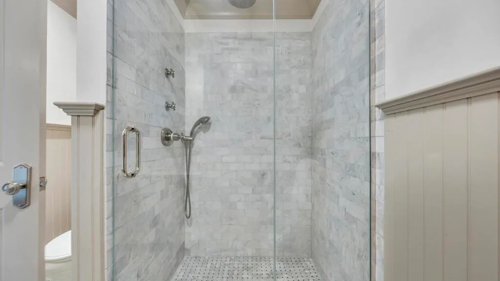 Una zona de ducha con azulejos, una mampara de vidrio y accesorios montados en la pared.