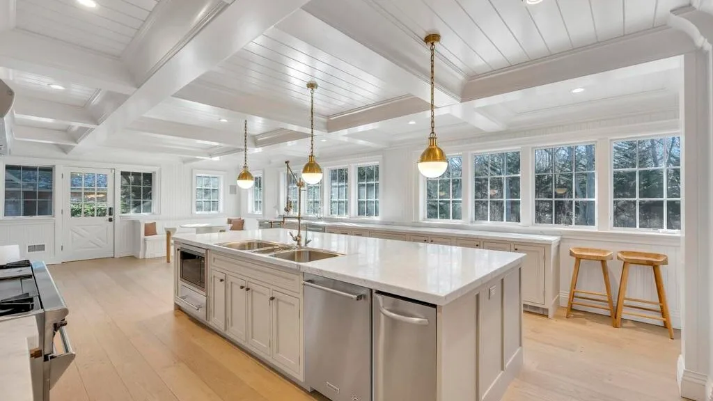 Una cocina luminosa con una gran isla, amplias ventanas y lámparas colgantes.