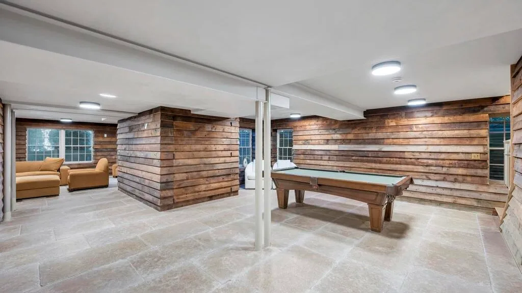 Una sala de recreación en el sótano con una mesa de billar, asientos y paredes revestidas de madera.