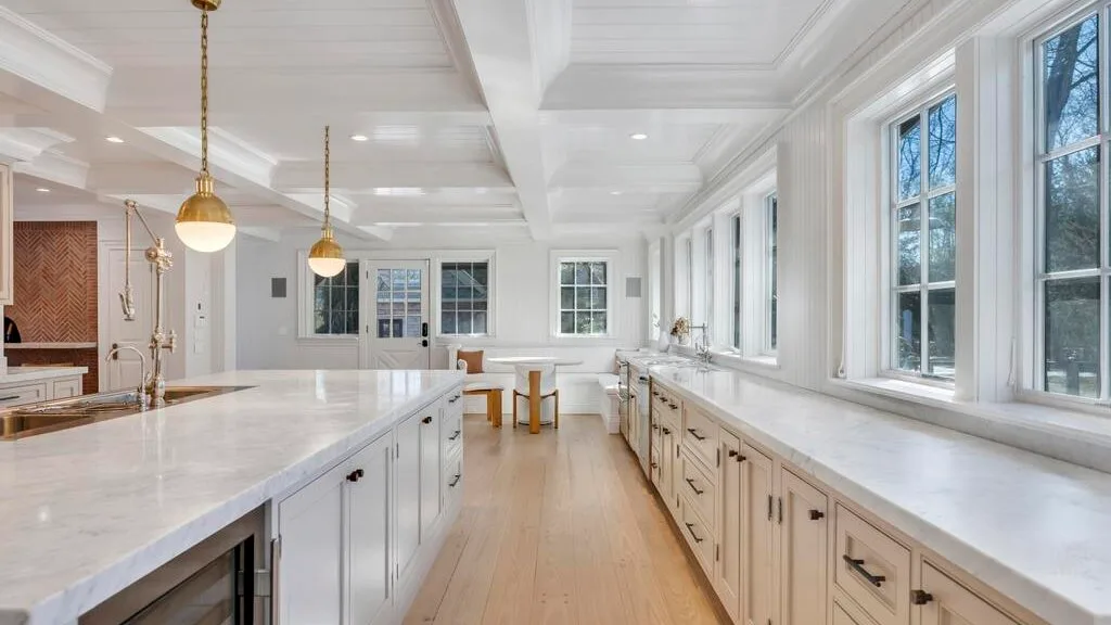 Una cocina luminosa con largas encimeras blancas, armarios y grandes ventanas.