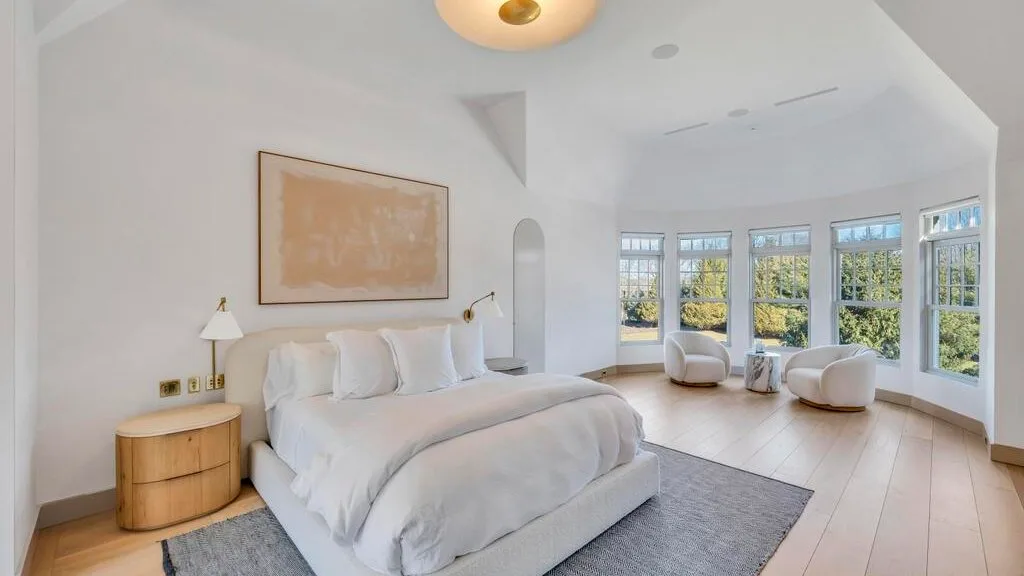 Un dormitorio luminoso con una cama grande y ventanas altas con vistas a la vegetación.