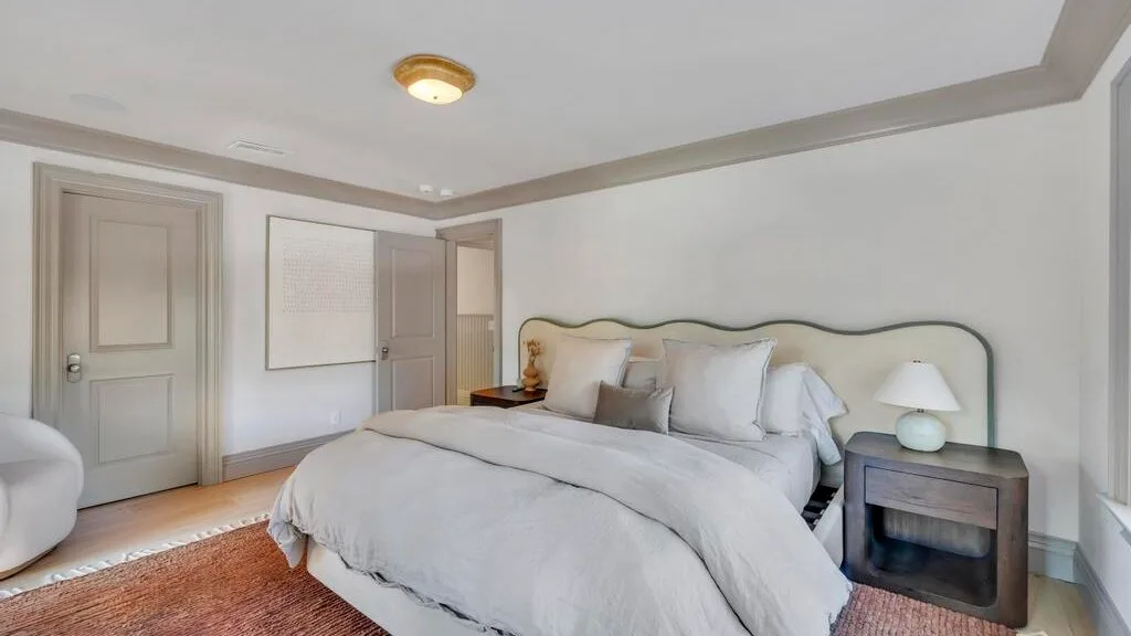 Un dormitorio con una cama grande, ropa de cama clara y una mesita de noche.