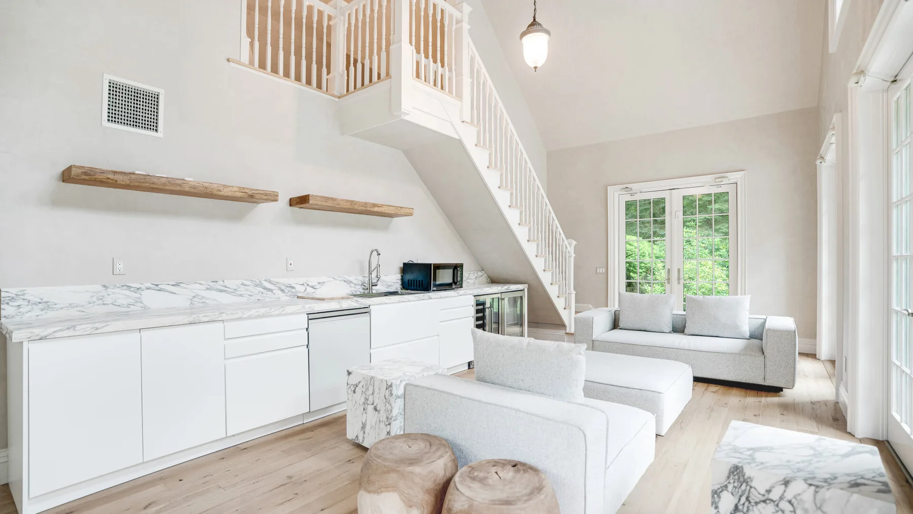 Una luminosa sala de estar abierta con cocina blanca y asientos bajo la escalera.