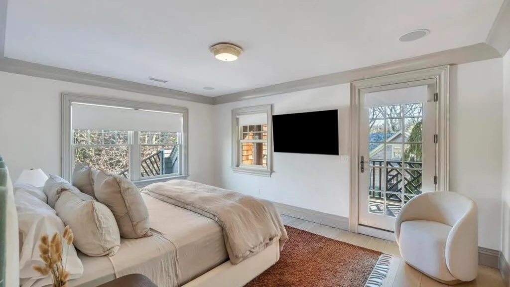 Un dormitorio luminoso con cama, televisor de pared y puerta de vidrio al balcón.