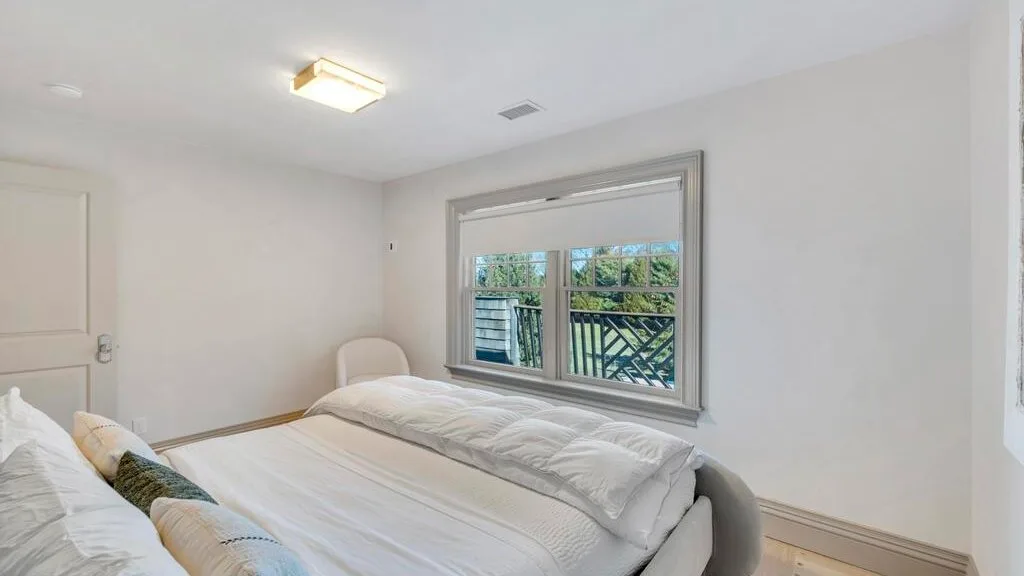 Un dormitorio luminoso con una cama junto a una ventana que da a la vegetación.