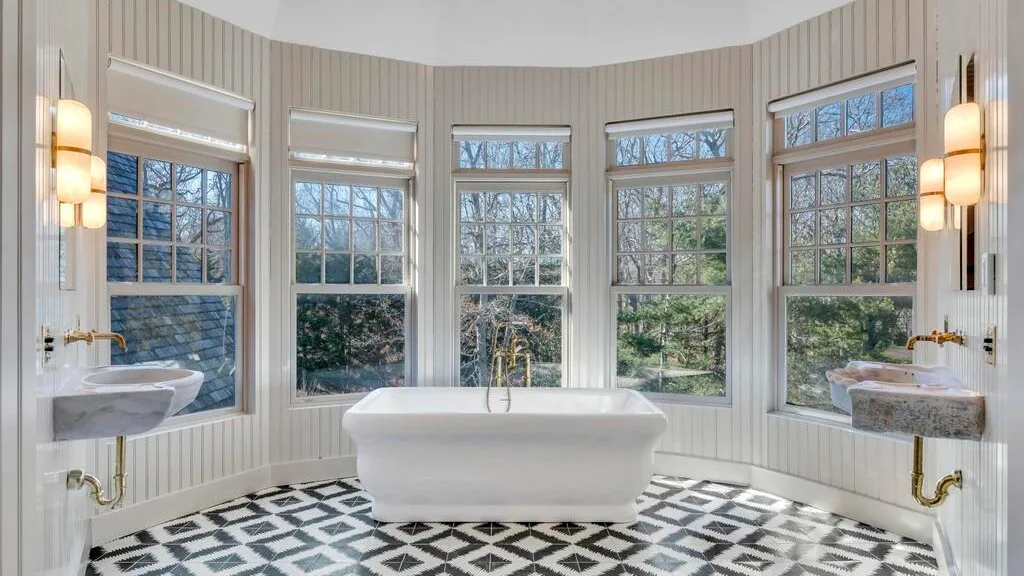 Un baño luminoso cuenta con una bañera exenta y varias ventanas grandes.
