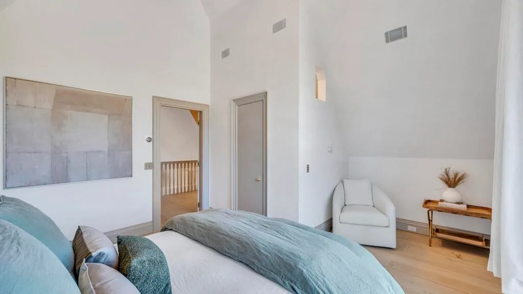 Un dormitorio luminoso con una cama, arte mural y una pequeña zona de estar.