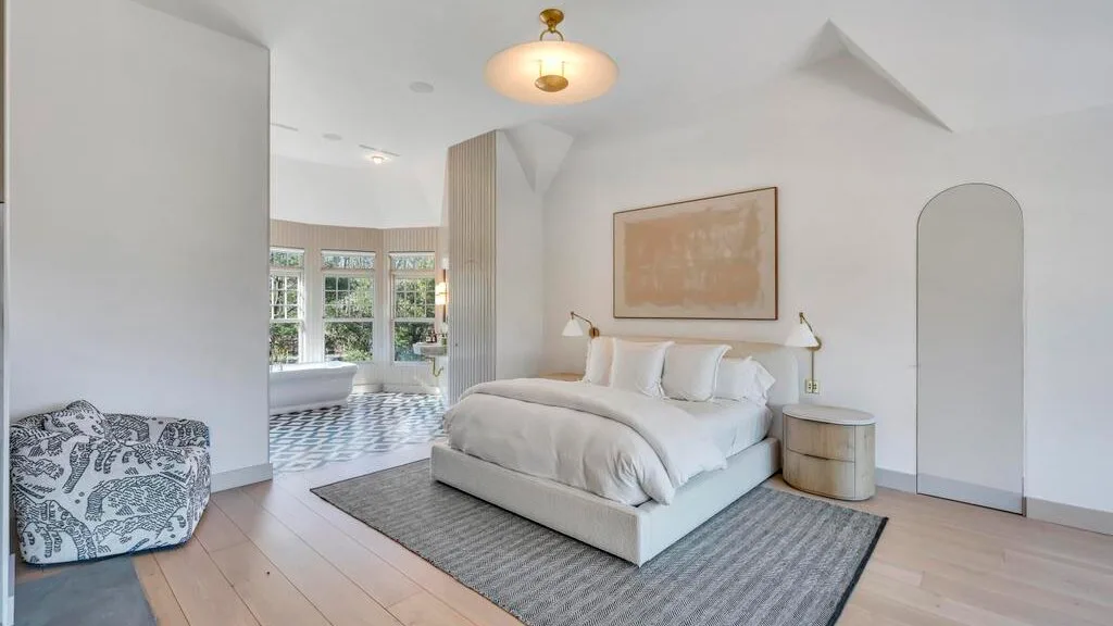 Un dormitorio luminoso con una cama, una alfombra y ventanas grandes.