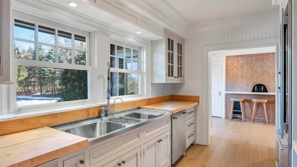 Una cocina luminosa con encimeras de madera, un fregadero y ventanas con vista a los árboles.