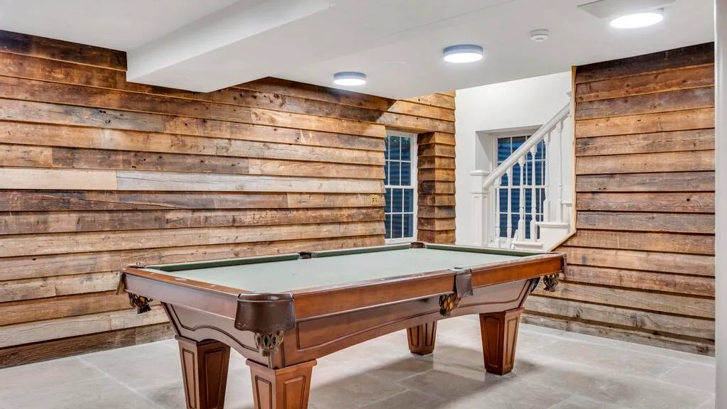 Una mesa de billar está en una habitación con paredes de tablas de madera y una escalera.