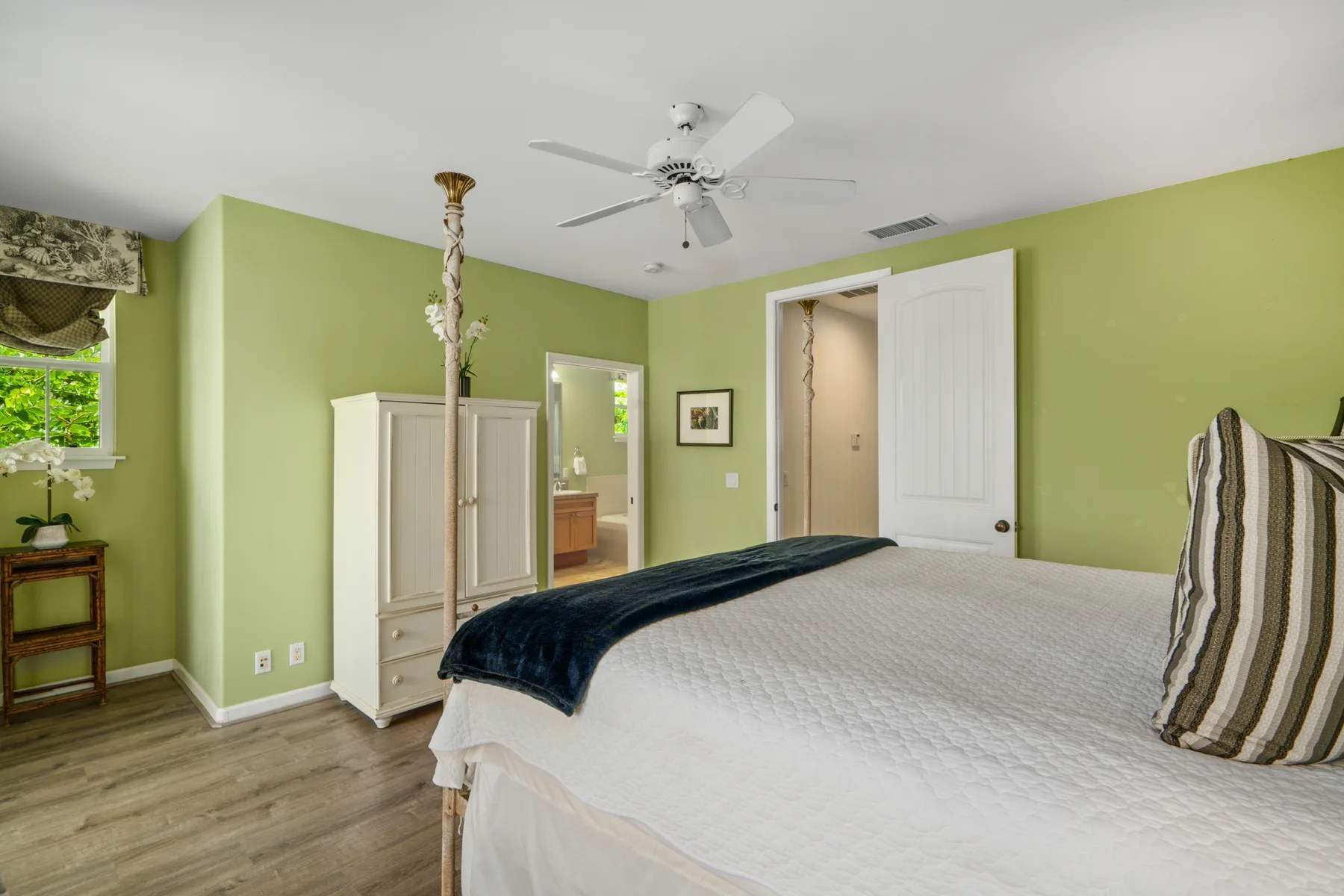 Un dormitorio con una cama grande, paredes verde claro y un ventilador de techo.