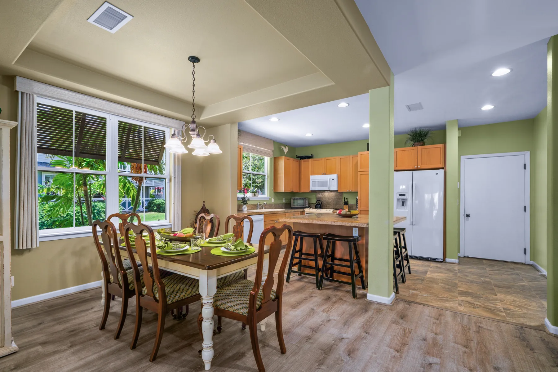 Comedor abierto junto a una cocina, con la mesa puesta y ventanas grandes.