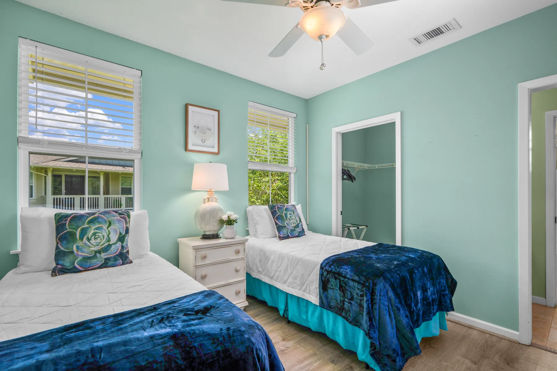 Un dormitorio con dos camas, ropa de cama azul y ventanas con persianas.