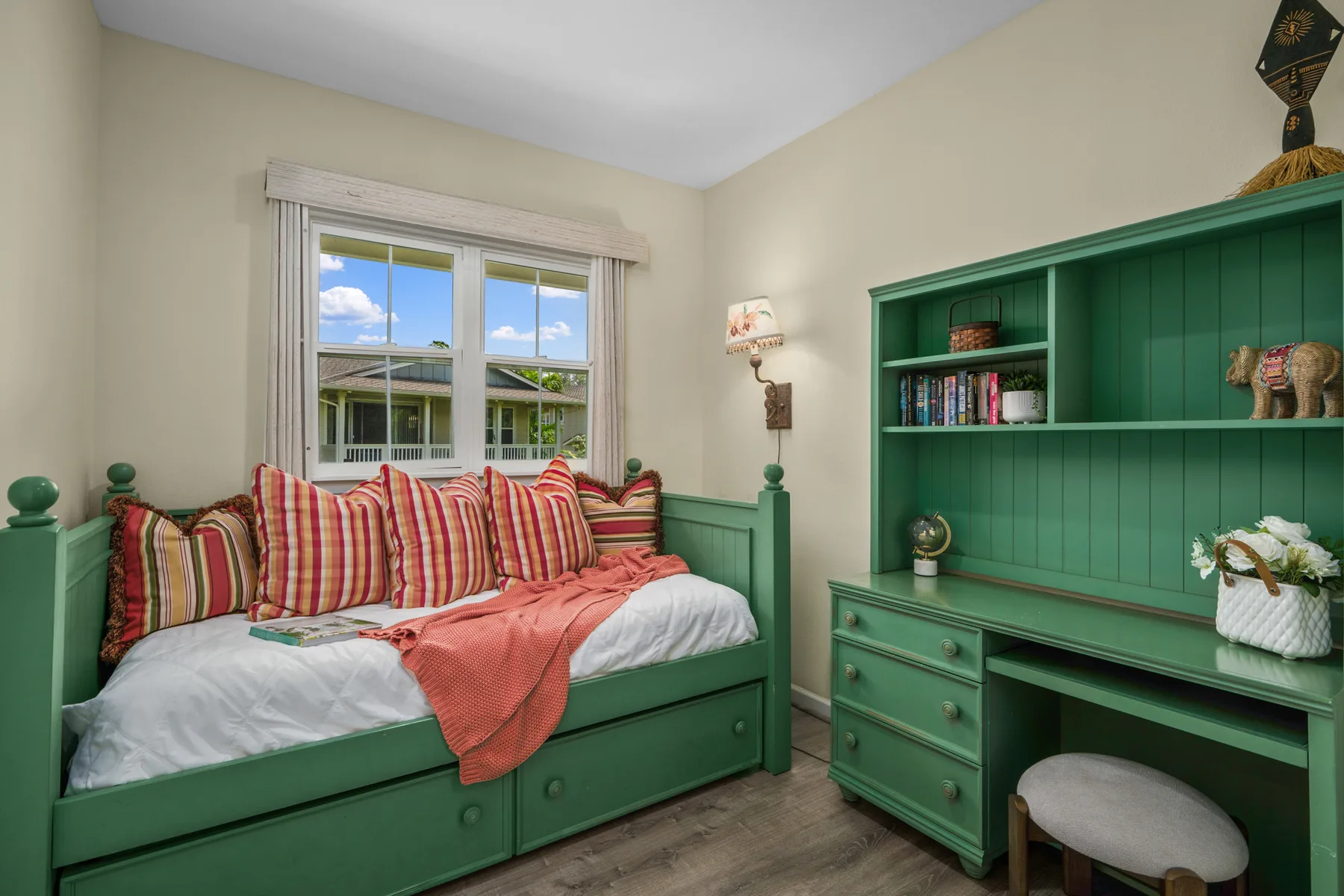 Una cama de día verde está junto a un escritorio y estantes empotrados en una habitación luminosa.