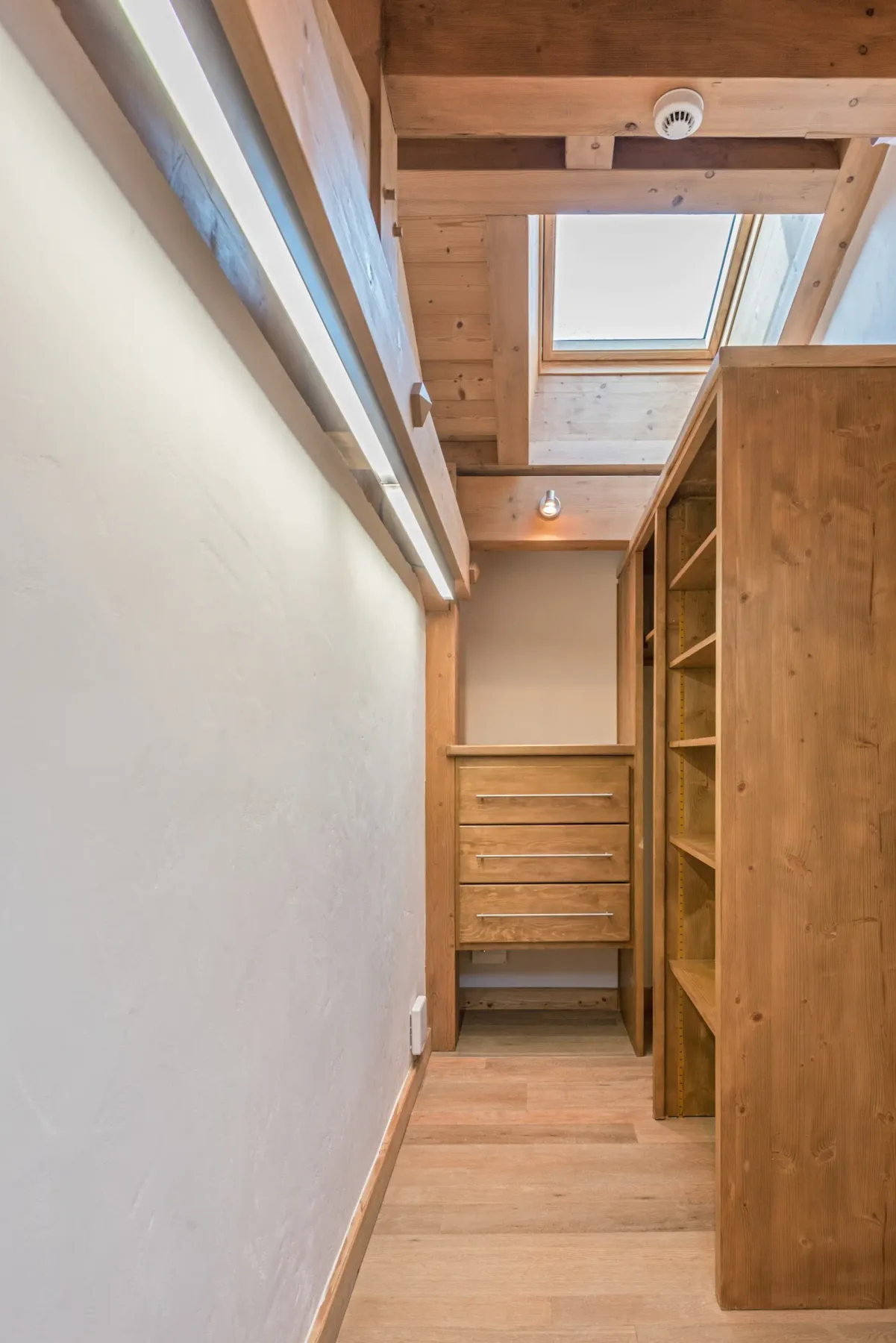 Un estrecho vestidor de madera con cajones empotrados y estanterías abiertas.