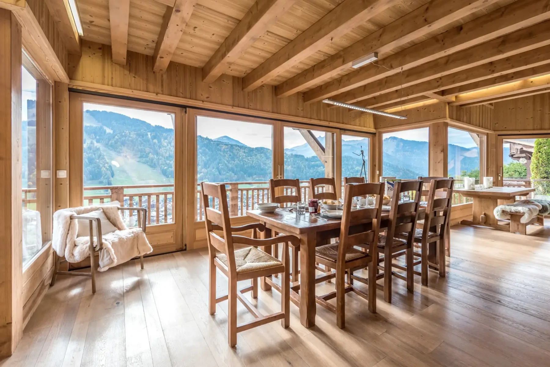 Una mesa de comedor de madera y asientos ocupan una sala luminosa con vistas a las montañas.