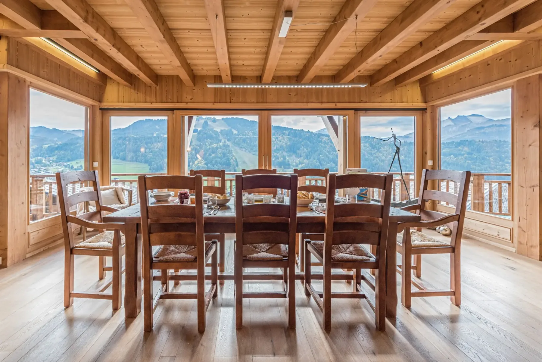 Una mesa de comedor de madera y sillas están frente a amplias ventanas con vistas a las montañas.