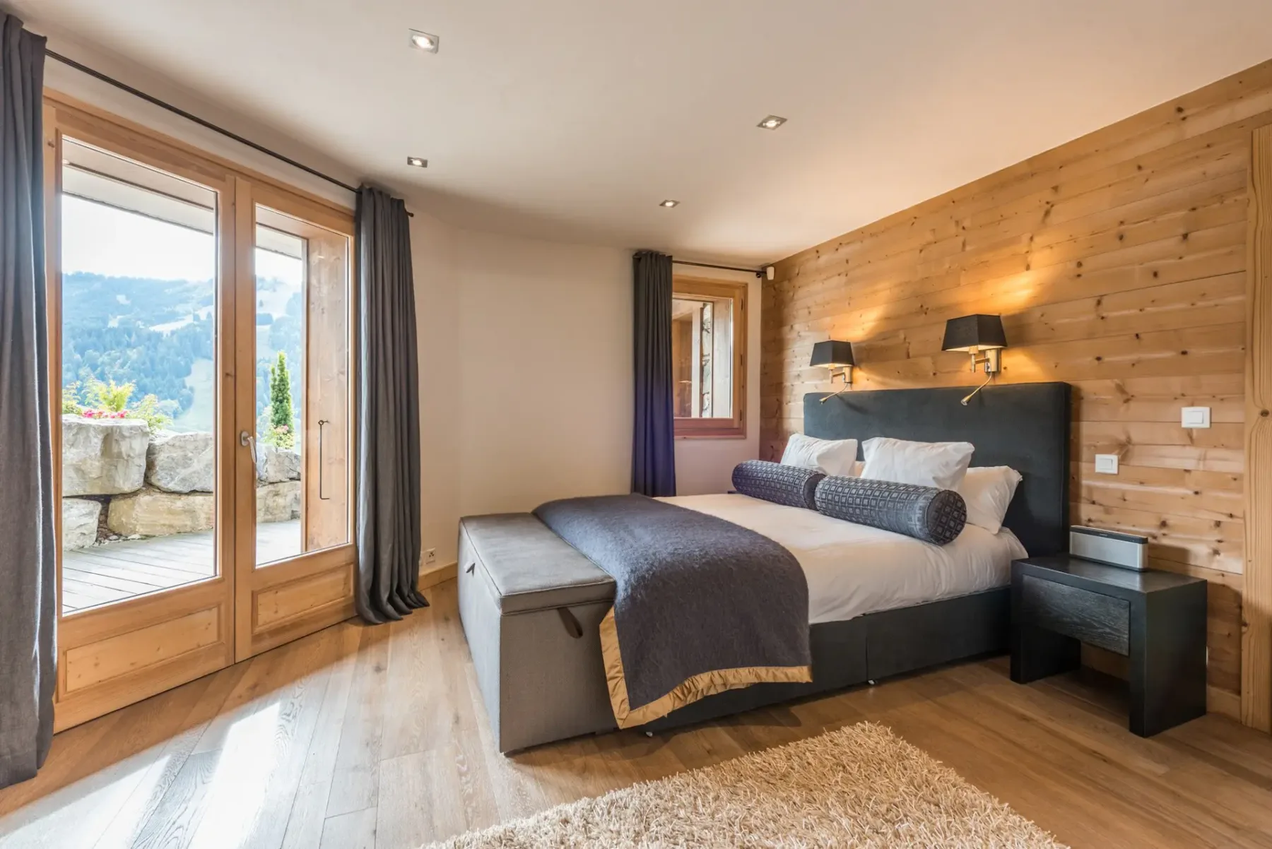 Un dormitorio con cama doble, pared revestida de madera y ventanas con vistas a las montañas.