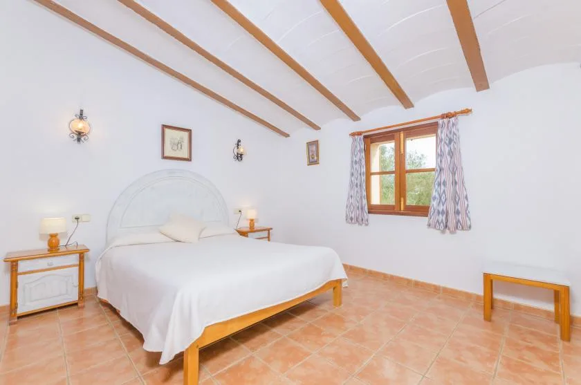 Un dormitorio con una cama blanca, vigas de madera a la vista y una ventana.