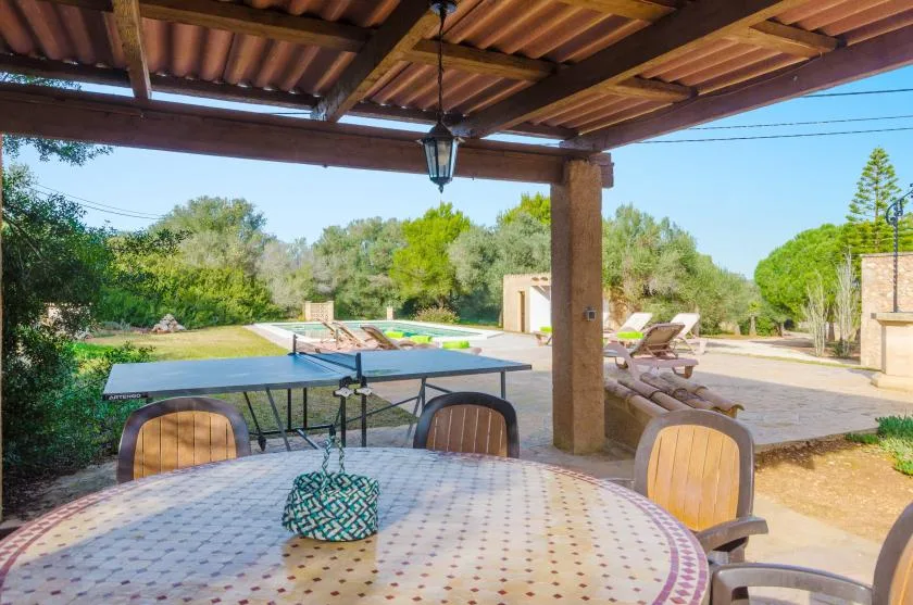 Una zona de comedor exterior cubierta da a un patio y una piscina.