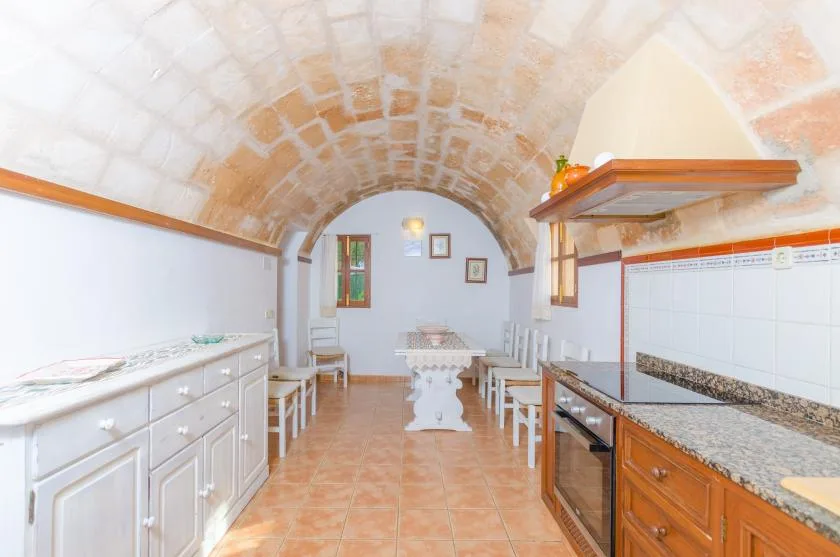 Una cocina con muebles blancos, una encimera de azulejos y un techo abovedado de ladrillo.