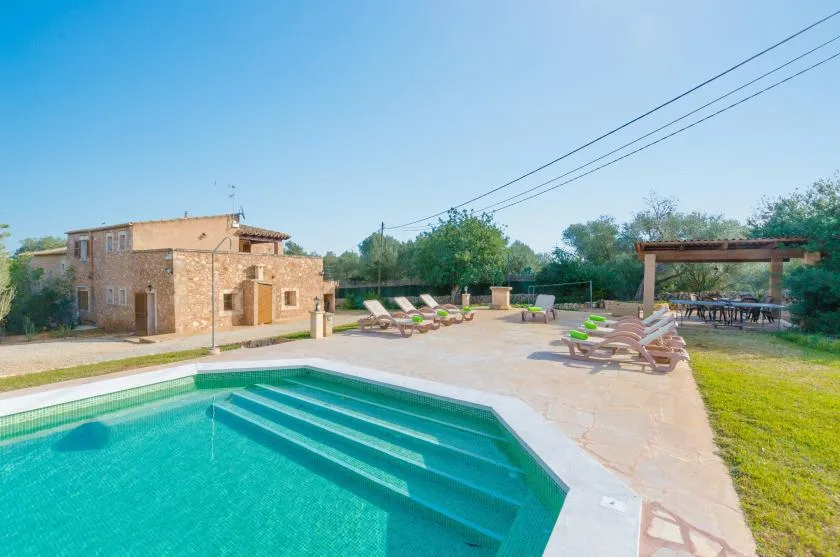 Una piscina al aire libre está junto a un edificio de piedra y un patio pavimentado con tumbonas.