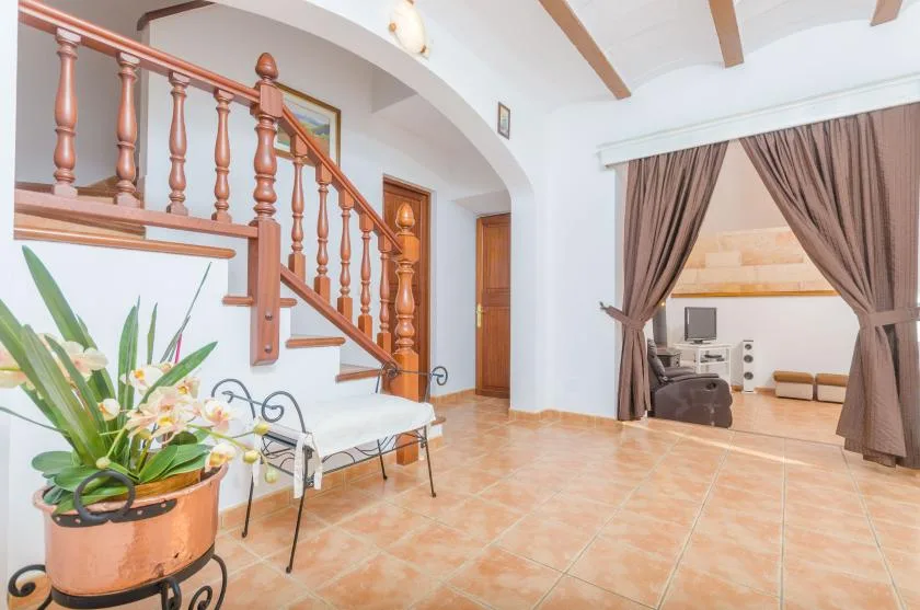 Interior con suelo de baldosas, una escalera y una abertura con cortinas hacia una sala de estar.