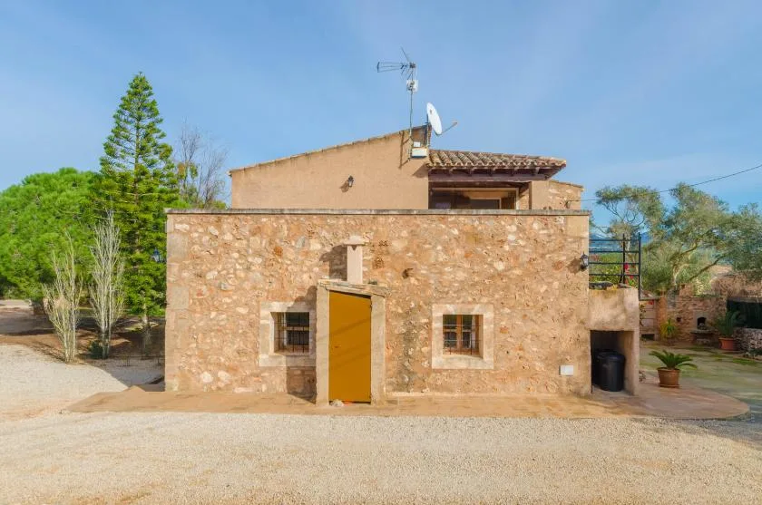 Una casa con fachada de piedra se encuentra junto a un patio de grava y árboles.