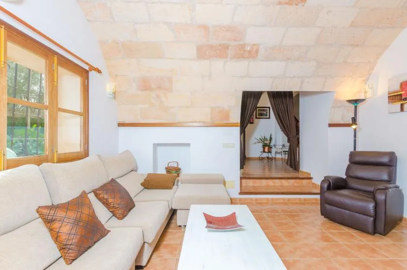 Una sala de estar con un sofá seccional claro, un sillón y una entrada a otra habitación.