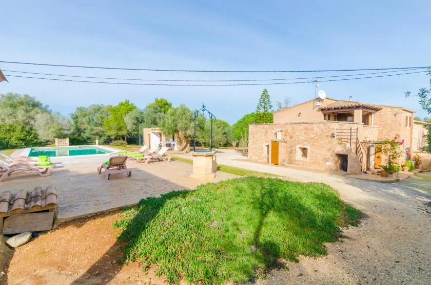 Una casa de piedra y una piscina están junto a un patio soleado con jardín.