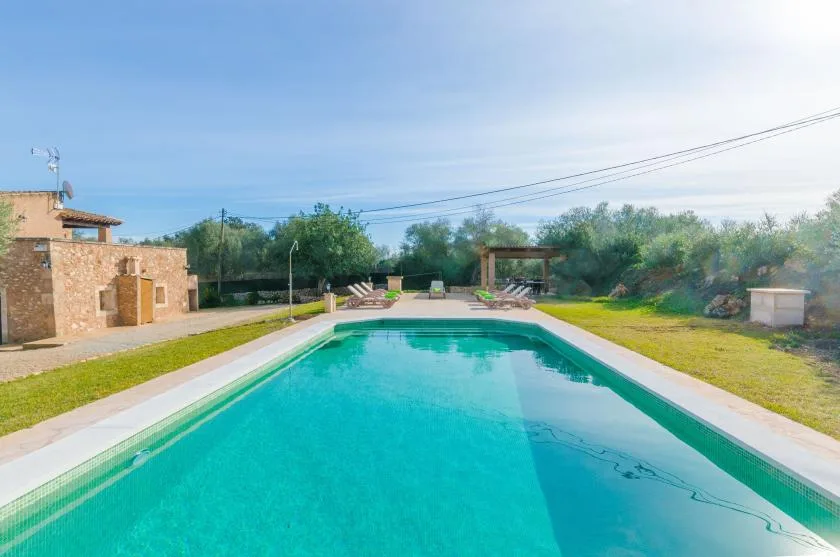 Una piscina al aire libre está junto a un edificio de piedra y un césped verde.