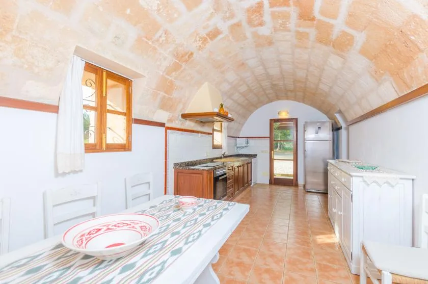 Cocina y comedor bajo un techo abovedado de ladrillo, con una mesa en primer plano.