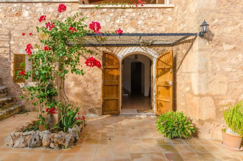 La entrada de un edificio de piedra da a un patio embaldosado con plantas en flor.