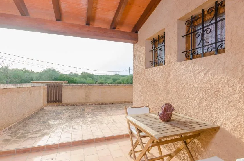 Una terraza cubierta con suelo de baldosas, mesa de madera y vistas a la vegetación.