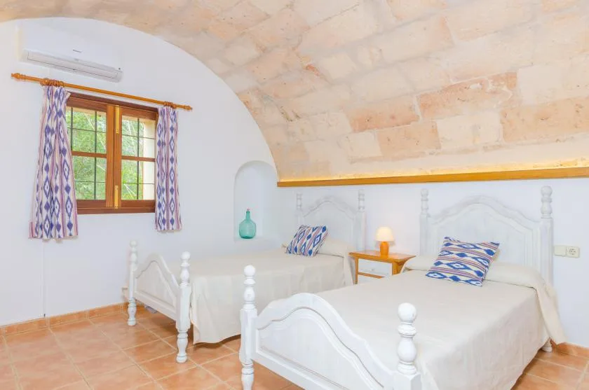 Un dormitorio con dos camas, una ventana y un techo curvo de piedra.