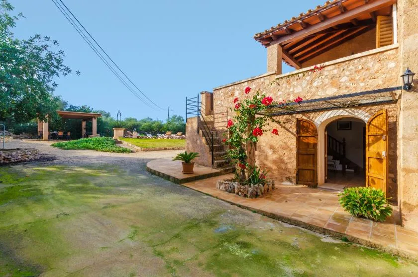 Un edificio de piedra con una entrada arqueada abierta y plantas con flores junto a un patio pavimentado.
