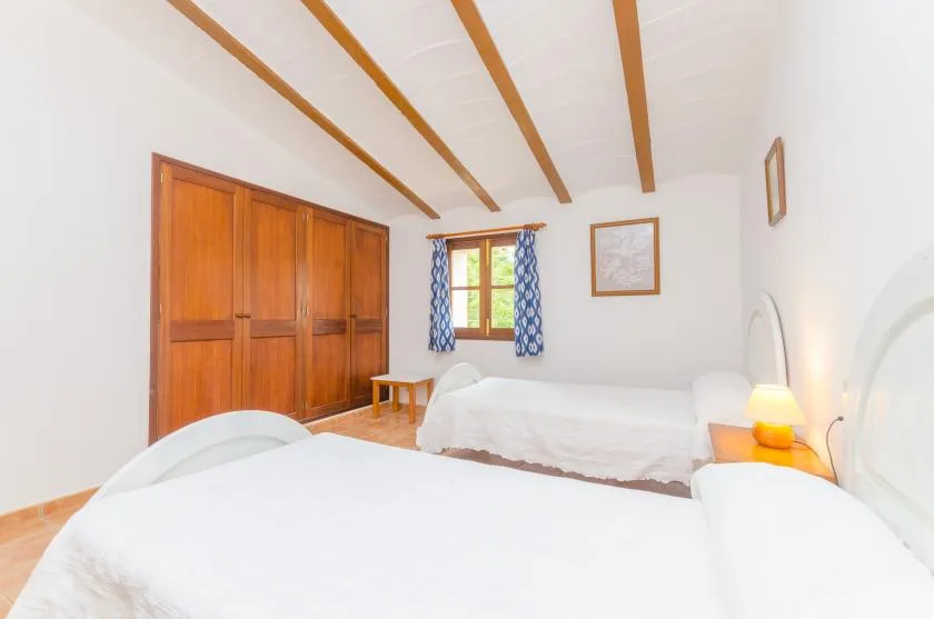 Un dormitorio luminoso con ropa de cama blanca, armarios de madera y una ventana con cortinas azules.
