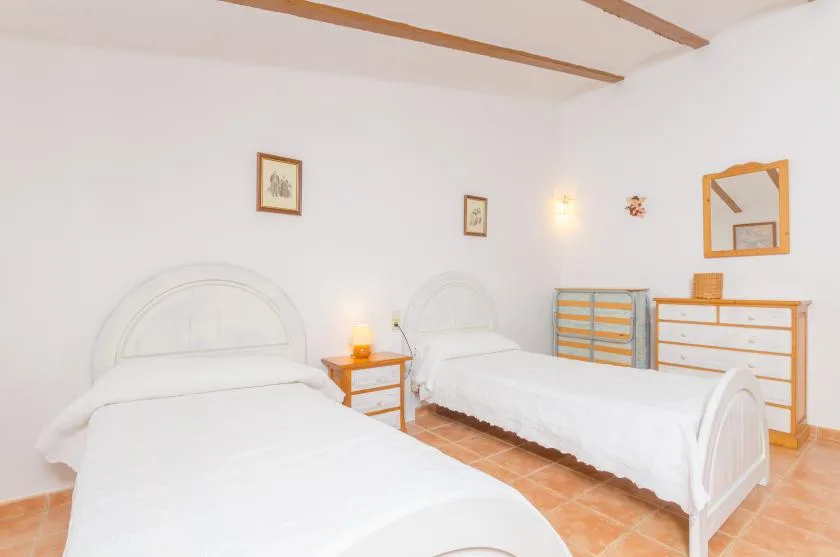 Un dormitorio luminoso con dos camas y cómodas de madera junto a una pared blanca.