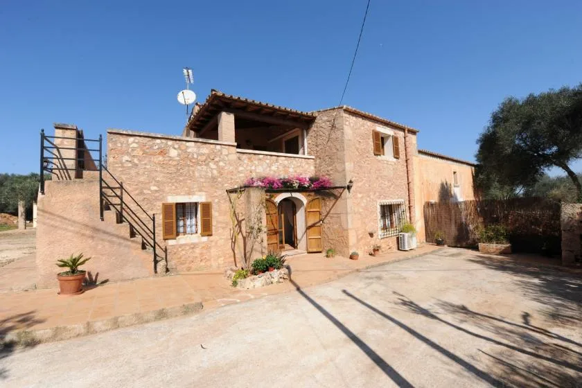 Una casa de piedra con una entrada cubierta de flores da a un patio soleado.