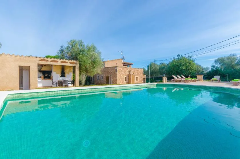 Una piscina al aire libre está junto a una casa de piedra y un patio cubierto.